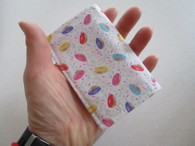 May include: A white fabric wallet with a donut and sprinkles pattern. The wallet is small and compact, perfect for carrying cards and cash.