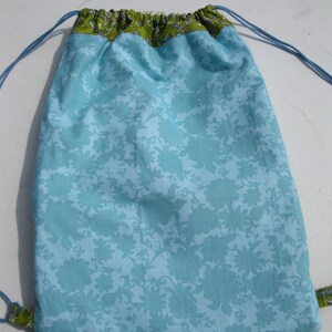 May include: A light blue drawstring bag with a green floral pattern. The bag has a white lining and a drawstring closure.