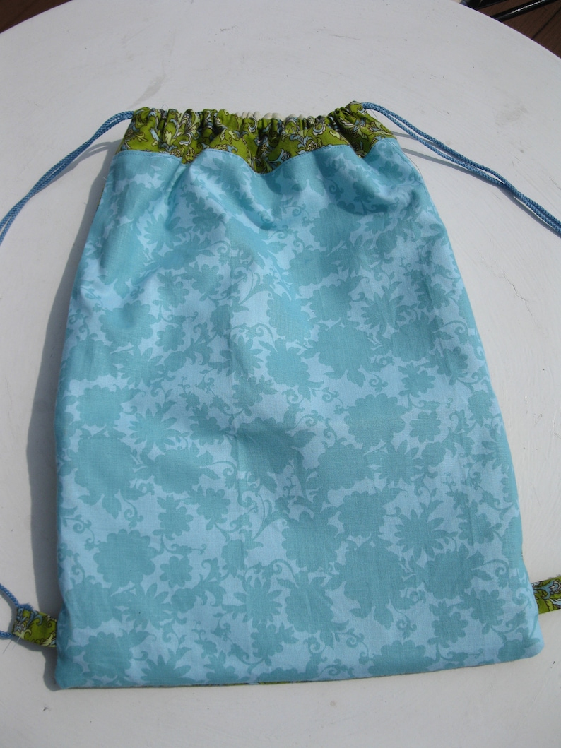 May include: A light blue drawstring bag with a green floral pattern. The bag has a white lining and a drawstring closure.