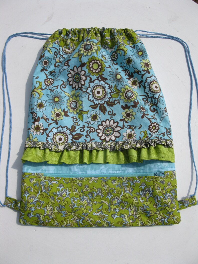May include: A blue and green drawstring bag with a floral pattern. The bag has a ruffled trim and a zippered pocket.