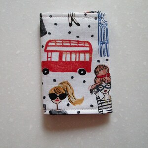 Puede incluir: Un porta tarjetas de tela blanca con un autob&uacute;s de dos pisos rojo, lunares negros e ilustraciones de mujeres con gafas de sol.