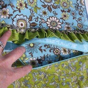May include: A blue and green fabric pouch with a zipper closure. The pouch is made of three layers of fabric, with a ruffled layer in the middle. The fabric has a floral pattern.