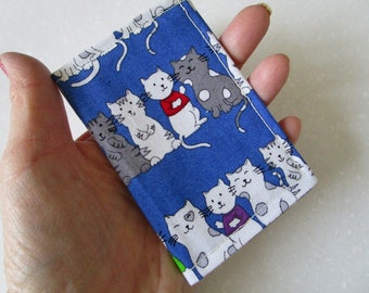 May include: A blue fabric pouch with a white stitched border. The pouch is decorated with a repeating pattern of white and gray cats with black eyes and whiskers. Some of the cats are wearing red, purple, or green clothing.