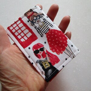 Puede incluir: Un porta tarjetas de tela blanca con una cabina telef&oacute;nica roja, lunares negros y dos mujeres de dibujos animados con vestidos rojos y gafas de sol.