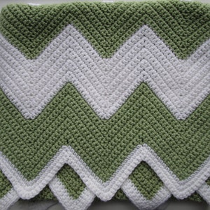 May include: A green and white chevron crochet baby blanket. The blanket is made with a soft, textured yarn and features a repeating chevron pattern.