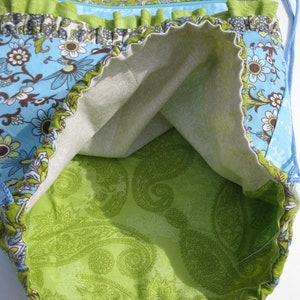 May include: A green and blue fabric drawstring bag with a paisley pattern lining. The bag has a ruffled trim and a zippered pocket.