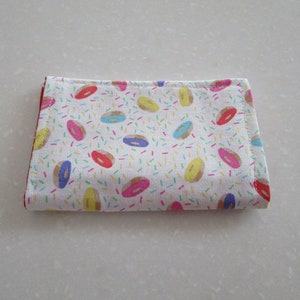May include: A white fabric pouch with a red border and a pattern of colorful donuts and sprinkles.