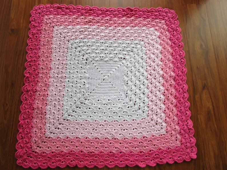 Pu&ograve; includere: Una copertina per neonati all'uncinetto con un centro bianco e un bordo sfumato rosa. La copertina &egrave; realizzata con un delicato motivo a punto e ha un bordo a festoni.