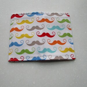 May include: A white fabric wallet with a colorful pattern of mustaches in various colors, including red, orange, yellow, green, blue, and gray.