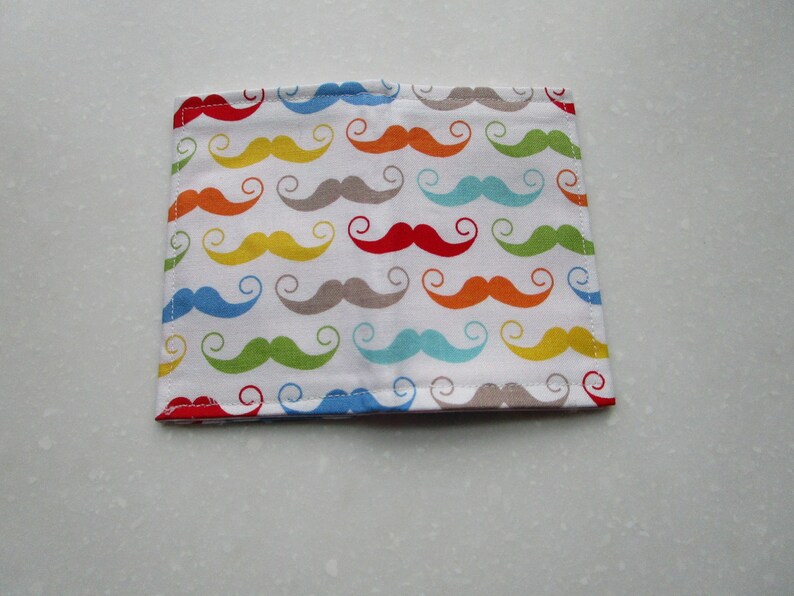 May include: A white fabric wallet with a colorful pattern of mustaches in various colors, including red, orange, yellow, green, blue, and gray.