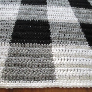 May include: A crocheted blanket with a black and white checkered pattern. The blanket is made with a variety of stitches, creating a textured look.