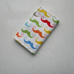 May include: A white fabric wallet with a colorful pattern of mustaches. The mustaches are in various colors, including red, yellow, blue, green, and orange.
