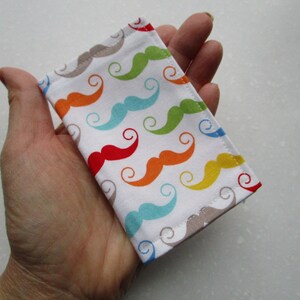 May include: A small white fabric pouch with a colorful mustache pattern. The pouch is made of cotton fabric and has a beige seam around the edges.