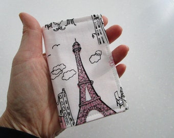 May include: A white fabric pouch with a pink and black illustration of the Eiffel Tower and other Parisian landmarks. The pouch has a pink and black stitched border.