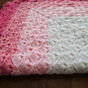 Pu&ograve; includere: Una copertina per neonati all'uncinetto con un design sfumato rosa e bianco. La copertina ha un bordo a scalare ed &egrave; realizzata con un delicato motivo a punto.