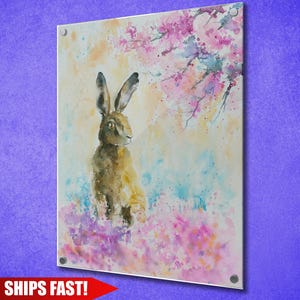 May include: Acrylic print featuring a watercolor painting of a hare in a field of colorful flowers. The artwork has a soft, dreamy quality with pastel colors and a touch of nature. The print is mounted on a clear acrylic panel.
