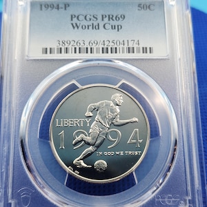 May include: A silver 1994 World Cup commemorative coin, graded PCGS PR69, encased in a clear protective holder. The coin features a soccer player in action, the word "LIBERTY", and the year "1994". The text "IN GOD WE TRUST" is also visible.