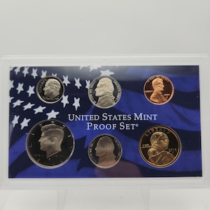 May include: A United States Mint Proof Set in a clear plastic case. The set includes six coins with portraits of historical figures. The background features a blue and white design with stars and stripes, and the text "UNITED STATES MINT PROOF SET®".
