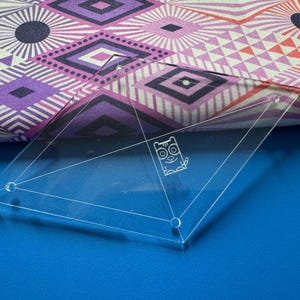 May include: A clear acrylic quilting ruler with a cat design. The ruler has a diamond shape with a triangle in the center. The ruler has three holes on the edges.