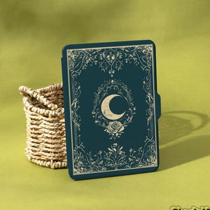 Può includere: Una custodia per tablet blu scuro con un design a mezzaluna e floreale. La custodia ha un bordo decorativo e un cestino intrecciato è a sinistra. Il marchio "Shadeify" si trova nell'angolo in basso a destra.