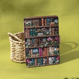 Könnte beinhalten: Eine dekorative Hülle mit einem Bücherregal-Design, das bunte Bücher und Blumen zeigt. Die Hülle ist braun mit einem Blumen- und Buchdesign. Ein geflochtener Korb befindet sich links von der Hülle auf einem grünen Hintergrund. Das Wort "Shadeify" befindet sich in der unteren rechten Ecke.