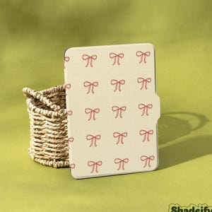 May include: A beige tablet case featuring a pattern of red bows. Beside it is a small woven basket. The word "Shadeify" is visible in the bottom right corner.