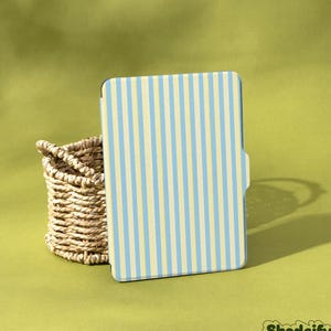 May include: A tablet case featuring a light blue and cream vertical stripe design. A woven basket is positioned to the left. The brand name "Shadeify" is visible in the bottom right corner.