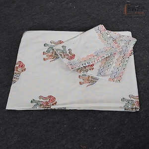 May include: A white cotton fabric featuring a repeating pattern of stylized elephants in red, green, and blue. The fabric includes a decorative border with a multi-colored zigzag design. The text SWER & shop is visible in the top right corner.