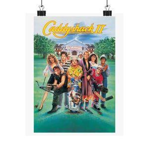 May include: A poster for the movie "Caddyshack II" featuring a group of people on a green golf course. The title is in yellow, with a white building in the background. The poster is held by two black binder clips.