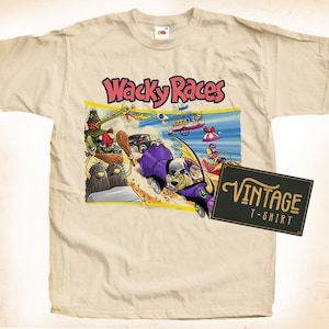 Może przedstawiać: Vintage'owa biała koszulka z nadrukiem kreskówkowych postaci z kreskówki Wacky Races. Na koszulce z przodu widnieje napis "Wacky Races" w kolorze czarnym. Obrazek przedstawia postacie w swoich samochodach, ścigające się na torze. Koszulka ma również vintage'ową metkę z napisem "Vintage T-Shirt" złotymi literami.