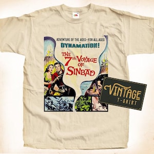 Peut inclure: Un t-shirt beige vintage avec un imprimé graphique du 7ème Voyage de Sinbad. Le graphique représente une scène du film avec une femme en robe rouge, un homme en chemise bleue et un grand navire. Le texte "Adventure of the Ages - For All Ages" et "Dynamation!" est imprimé au-dessus du graphique. Le texte "Vintage T-Shirt" est imprimé sur un rectangle noir dans le coin inférieur droit.