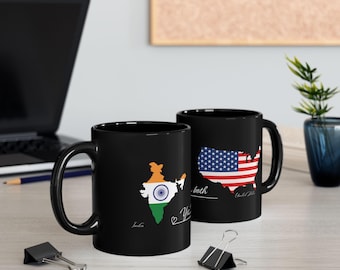 Op de afbeelding: Twee zwarte keramische mokken. Eén mok heeft een kaart van India met de kleuren van de Indiase vlag en het woord "India". De andere mok heeft een kaart van de Verenigde Staten met het ontwerp van de Amerikaanse vlag en de woorden "Verenigde Staten".