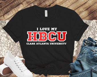 Może przedstawiać: Czarny T-shirt z białym tekstem, który brzmi "I love my HBCU Clark Atlanta University". Tekst jest w czerwonej czcionce blokowej.