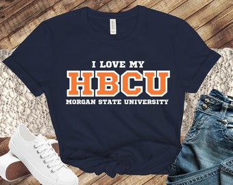 May include: Navy blue t-shirt with white text that reads "I love my HBCU Morgan State University". The text "HBCU" is in orange and outlined in white.