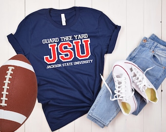 May include: A navy blue t-shirt with the text "GUARD THEE YARD JSU JACKSON STATE UNIVERSITY" in white and red lettering. A brown football, blue jeans, and white sneakers are also pictured.