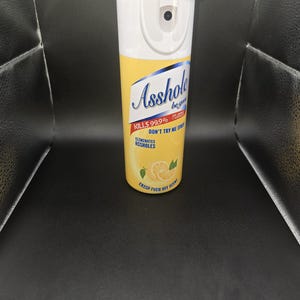 K&ouml;nnte beinhalten: Ein wei&szlig;-gelber Isolierbecher mit Deckel. Der Becher tr&auml;gt den Schriftzug "Asshole" in blauer Schrift sowie die S&auml;tze "Kills 99.9%", "Don't Try Me Spray" und "Eliminates Assholes". Au&szlig;erdem steht dort "Crisp Fuck Off Scent".