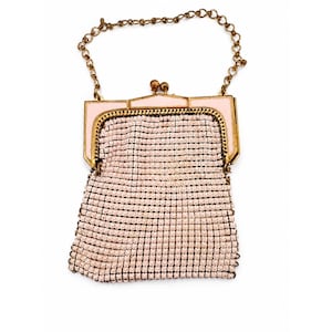May include: A small handbag featuring a pale pink mesh body and a gold-tone metal frame. The bag has a matching pale pink enamel top bar with a dual-ball clasp closure and a thin gold-tone chain handle attached to the sides of the frame.