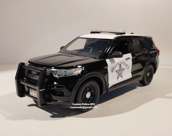 May include: Black and white police car model with a black grill, a black bumper, and a black roof. The car has a white star and the words "Elgin Police" on the side. The car is on a white surface.