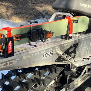 May include: A snowmobile with skis attached. The skis are green and orange, secured by red and black brackets. The snowmobile is silver and black, with the word "Polaris" visible.