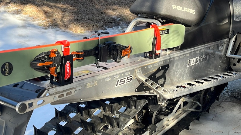 May include: A snowmobile with skis attached. The skis are green and orange, secured by red and black brackets. The snowmobile is silver and black, with the word "Polaris" visible.
