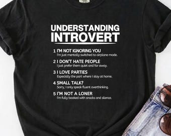 Puede incluir: Una camiseta negra de manga corta con el texto blanco UNDERSTANDING INTROVERT seguido de una lista numerada de cinco puntos que explican la introversión. La camiseta tiene cuello redondo y se combina con pantalones cortos de mezclilla.
