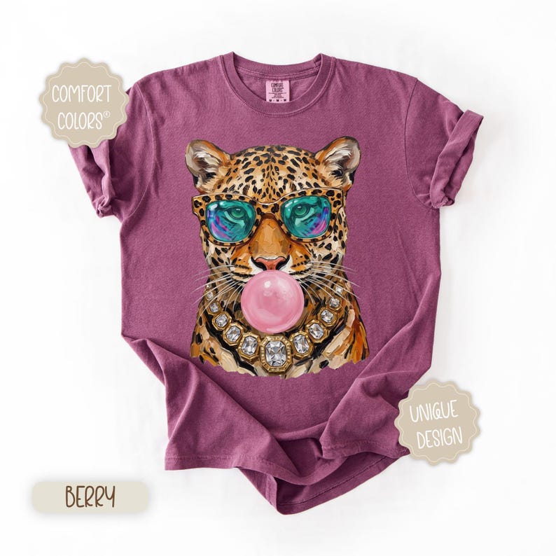 May include: Berry-colored t-shirt featuring a leopard wearing sunglasses and a jeweled necklace, blowing a bubblegum bubble. The shirt has the words "Comfort Colors" and "Unique Design" on it.