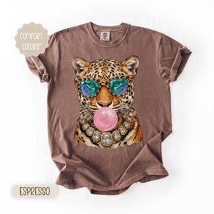 May include: Espresso-colored t-shirt featuring a leopard wearing sunglasses and blowing a bubblegum bubble. The leopard has a jeweled necklace. The shirt has the words "Comfort Colors" and "Espresso" printed on it.