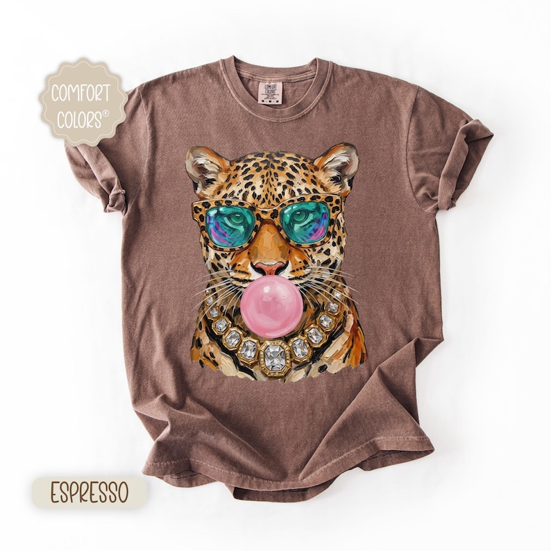 May include: Espresso-colored t-shirt featuring a leopard wearing sunglasses and blowing a bubblegum bubble. The leopard has a jeweled necklace. The shirt has the words "Comfort Colors" and "Espresso" printed on it.
