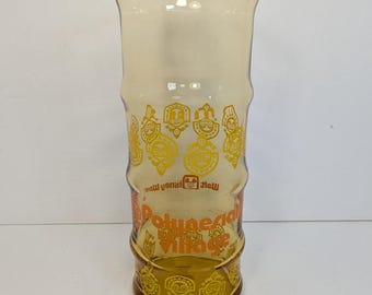 Op de afbeelding: Een hoog, amberkleurig glas met een bamboe-achtige textuur. Het is voorzien van gele grafische prints van tiki-maskers en de tekst "Polynesian Village" in het oranje, samen met het "Walt Disney World"-logo in het bruin.