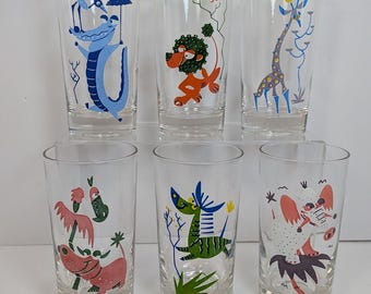 Op de afbeelding: Set van zes vintage heldere drinkglazen. Elk glas heeft een andere cartoon dierenillustratie in heldere kleuren, waaronder een krokodil, een leeuw, een giraffe, een flamingo en een muis. De glazen zijn cilindrisch.