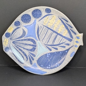May include: A ceramic serving platter with a speckled gray background and a fish-shaped design. The platter features blue, light blue, and yellow abstract patterns. The platter has two small handles on either side.