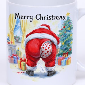 Op de afbeelding: Witte keramische mok met een humoristisch kerstontwerp. De mok toont de kerstman die zich bukt, met zijn rode pak en een hartvormig ontwerp op zijn achterwerk. De woorden "Merry Christmas" staan op de mok.
