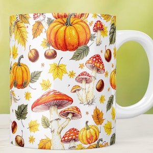 Può includere: Tazza in ceramica bianca con un motivo autunnale colorato. Il design presenta zucche arancioni, funghi con cappello rosso, foglie gialle e castagne marroni. La tazza ha un manico bianco ed è ambientata su uno sfondo verde sfocato.