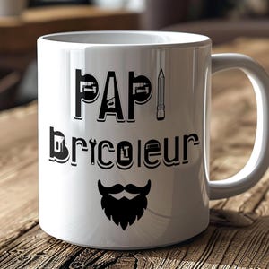 Peut inclure: Mug en céramique blanche avec l'inscription noire "PAPI Bricoleur", un dessin de crayon et une moustache et barbe stylisées. Le mug est posé sur une surface en bois.